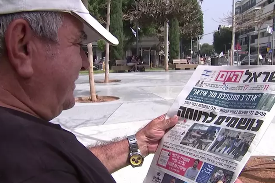 Homem usa boné branca e camiseta preta está lendo jornal